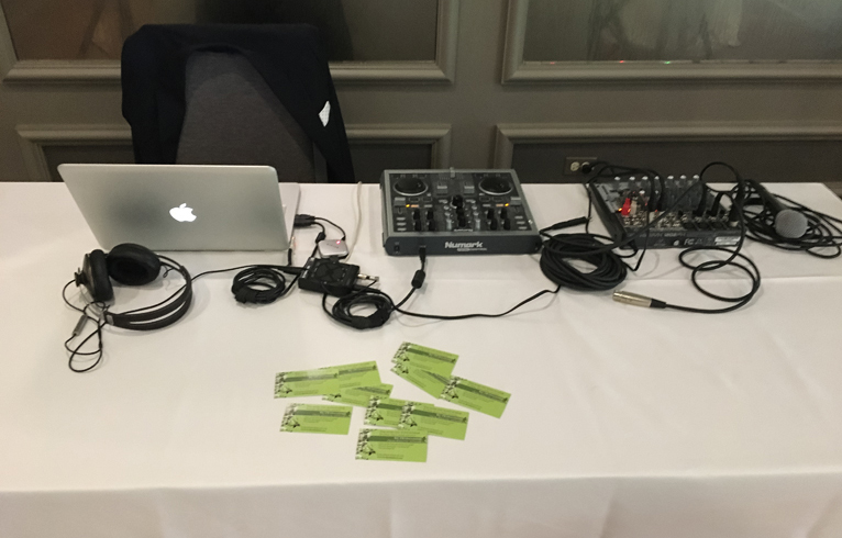 DJ table showing laptop, business cards, headphones, controller, microphone, and mixer